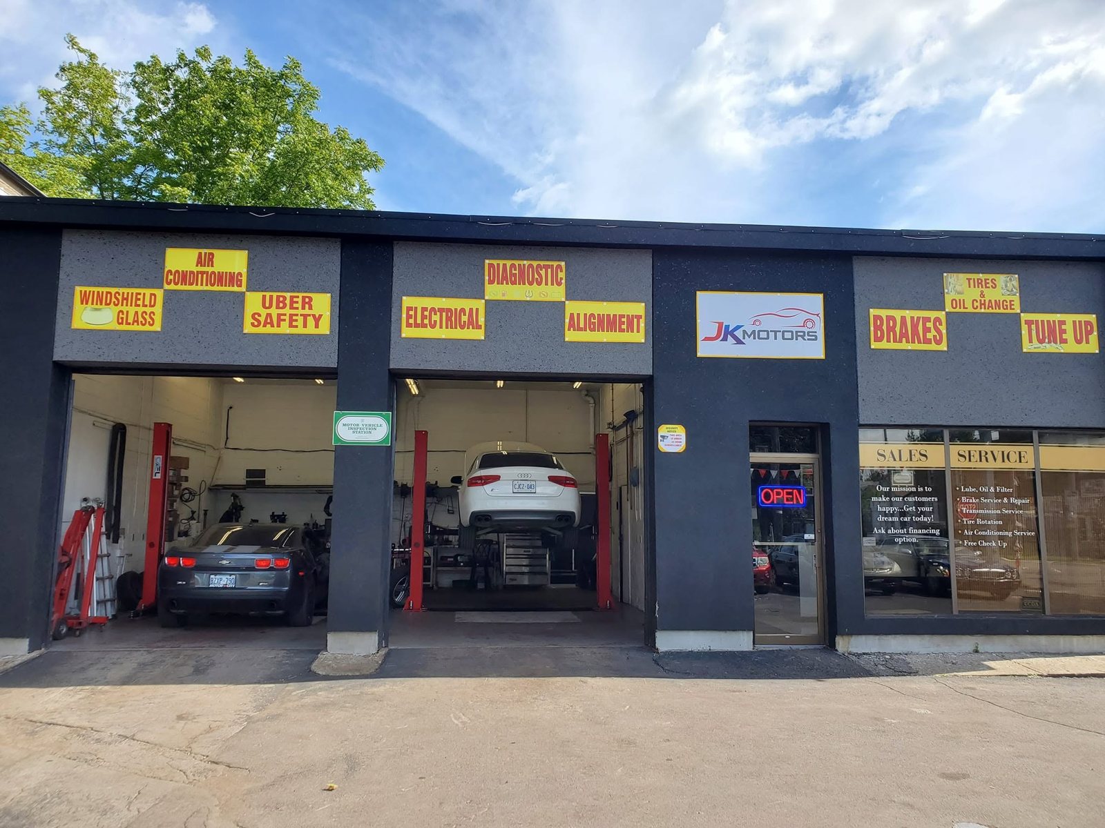 The JK Motors shopfront at 230 King St, Welland, with open service bays, cars on the lifts, and a licensed Motor Vehicle Inspection Station sign